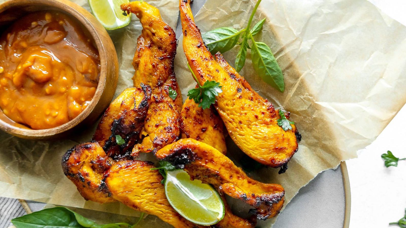 air fryer chicken satay on a platter with thai basil and limes