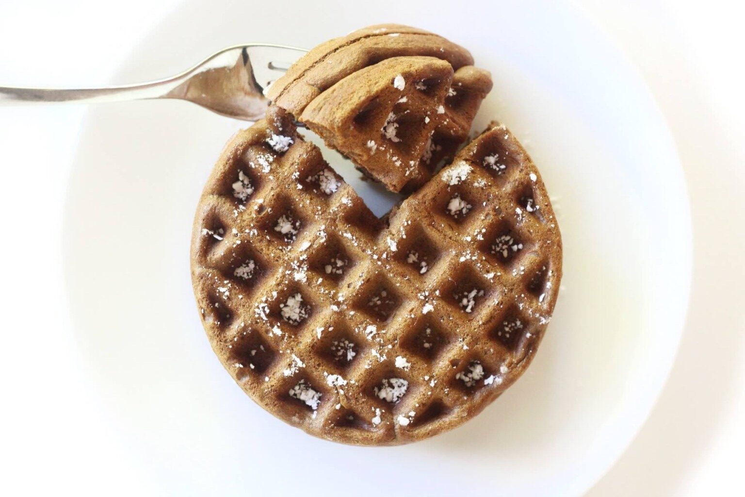 A fork holding a piece of Gingerbread Waffle on a plate.
