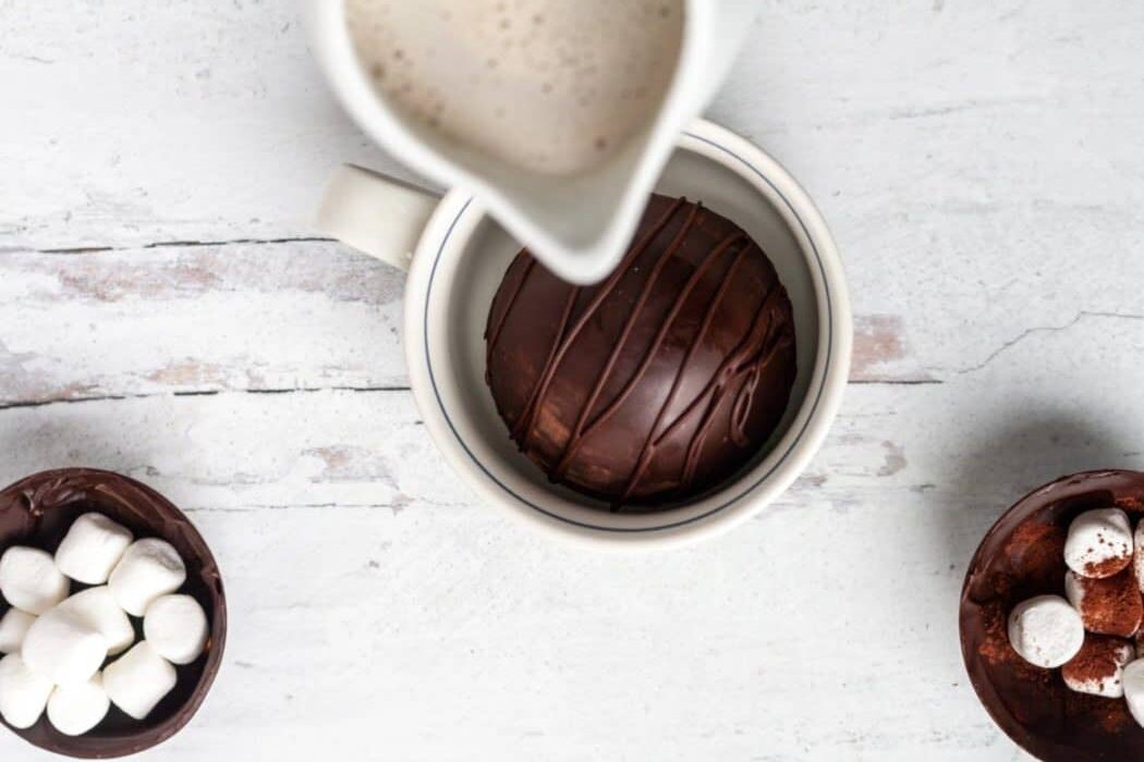 A small pitcher pouring milk into a mug with a Hot Cocoa Bomb inside.