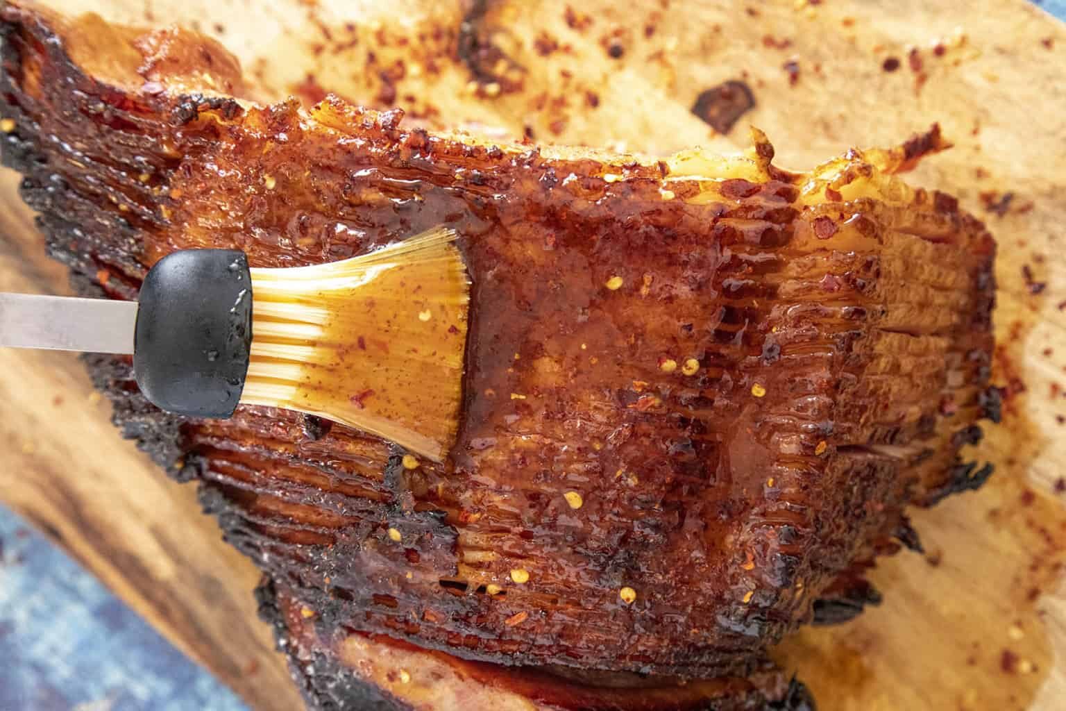 A pastry brush brushing Hot Honey Glaze on Ham