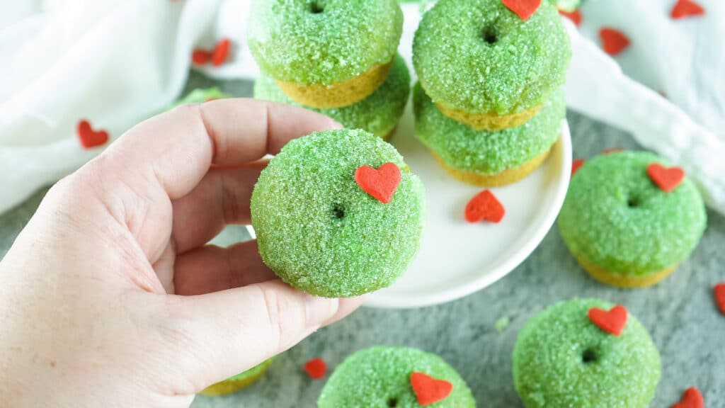 A hand holding up a Grinch Donut over a plate full of donuts