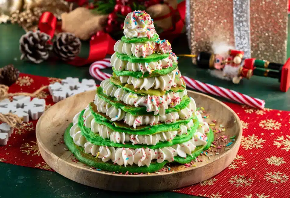 A tray of green stacked pancakes with whipped cream and sprinkles to look like a Christmas Tree.