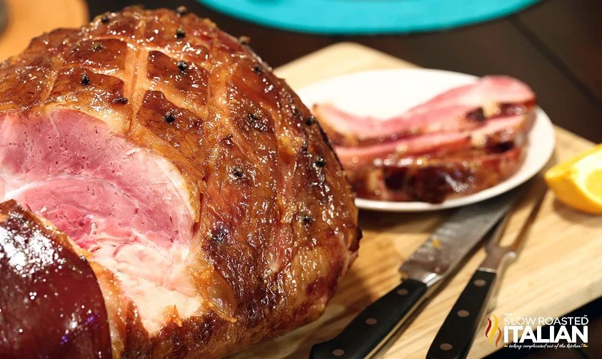 A close up of an Orange Honey Glazed Ham with cut up ham on a plate.