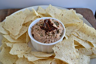 A small bowl of Black Eyed Pea Hummus with chips surrounding it.