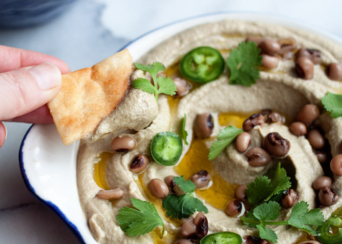A chip dipped into a bowl of Jalapeno Black-Eyed Pea Hummus.