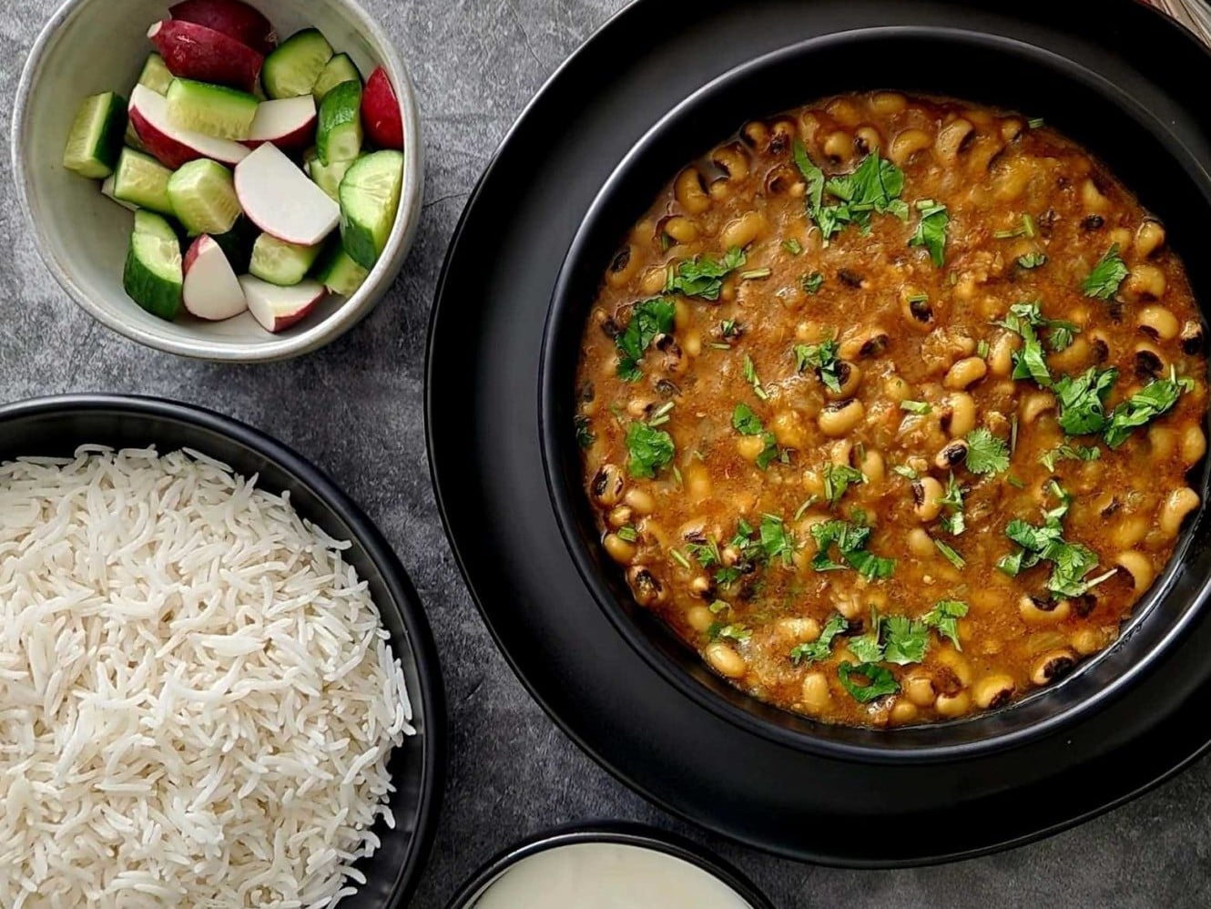 An overhead shot of Black Eyed Peas Curry with bowls of rice and vegetables on the side.