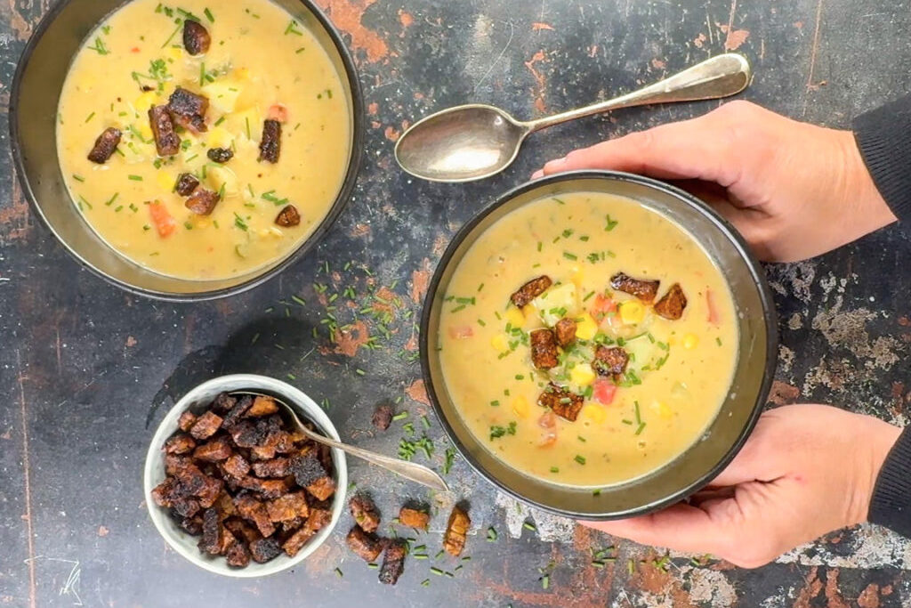An overhead shot of hands holding a bowl of Corn and Potato Chowder (with Tempeh Bacon)