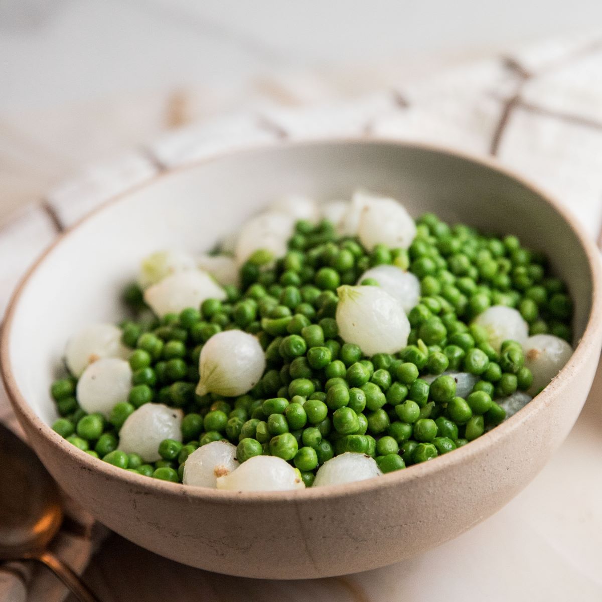 Beige bowl with peas and pearl onions.