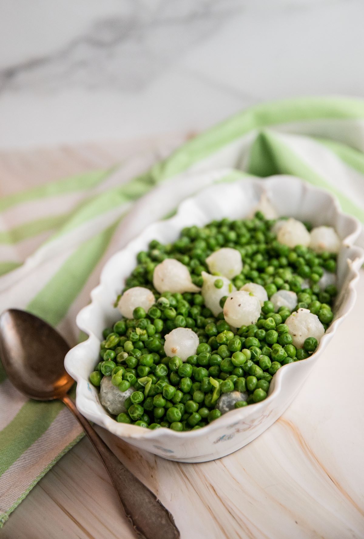 Peas and pearl onions in a white bowl with a stripped kitchen towel.