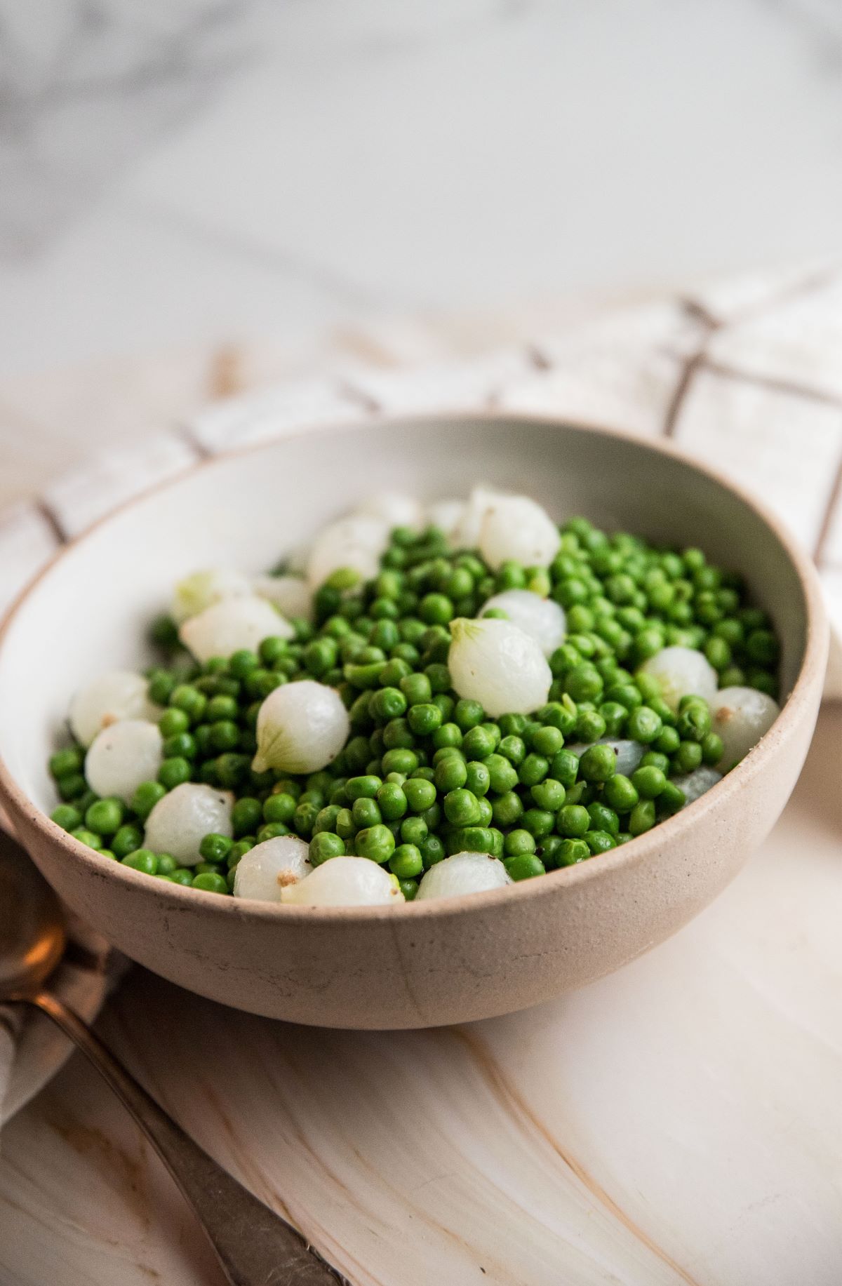 Peas and pearl onions in a beige bowl.