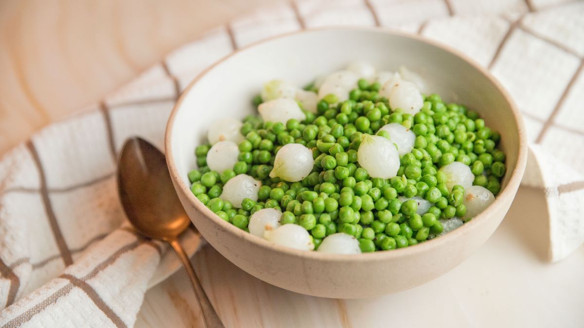 Beige bowl filled with peas and pearl onions.