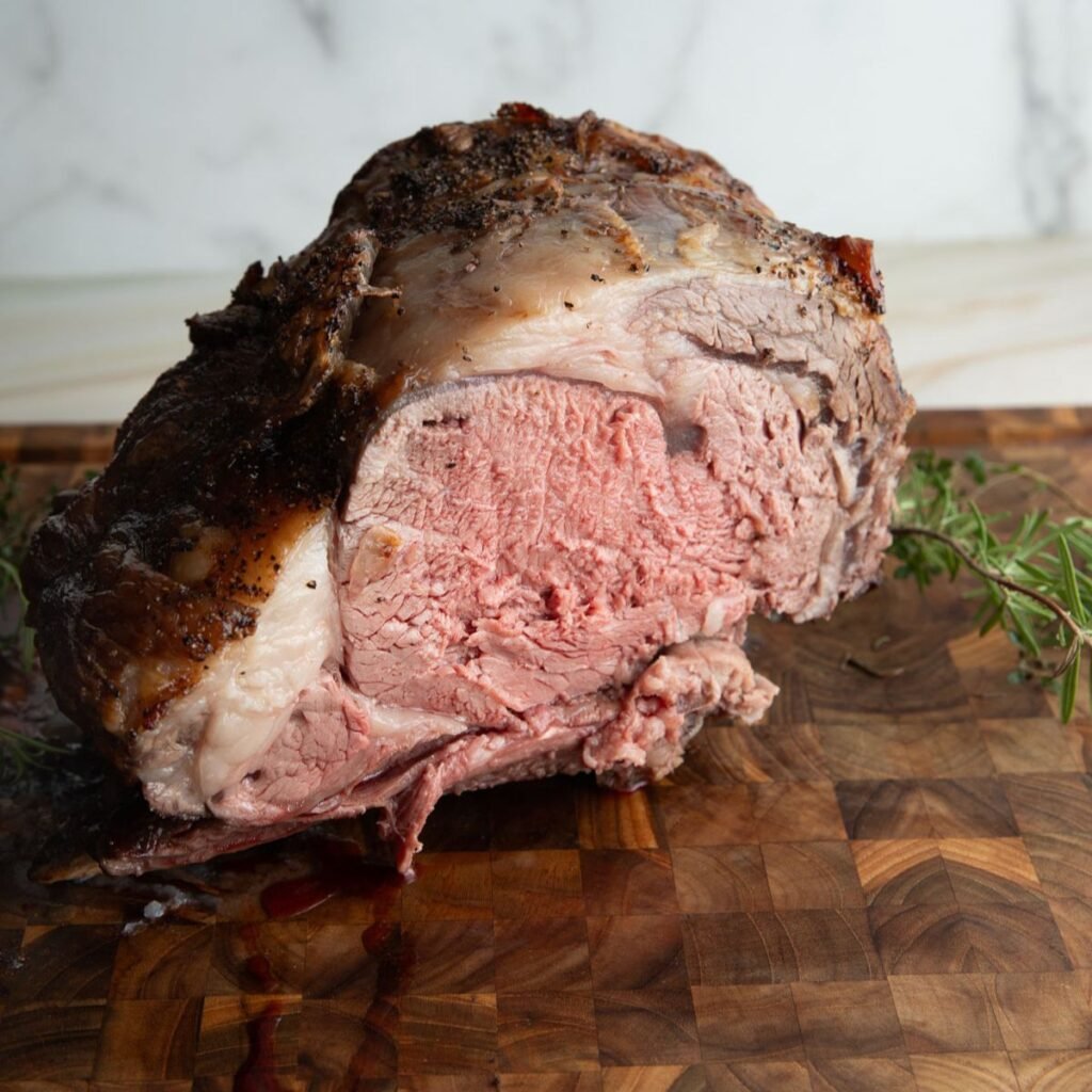 Sliced prime rib roast on a wooden cutting board with herbs.