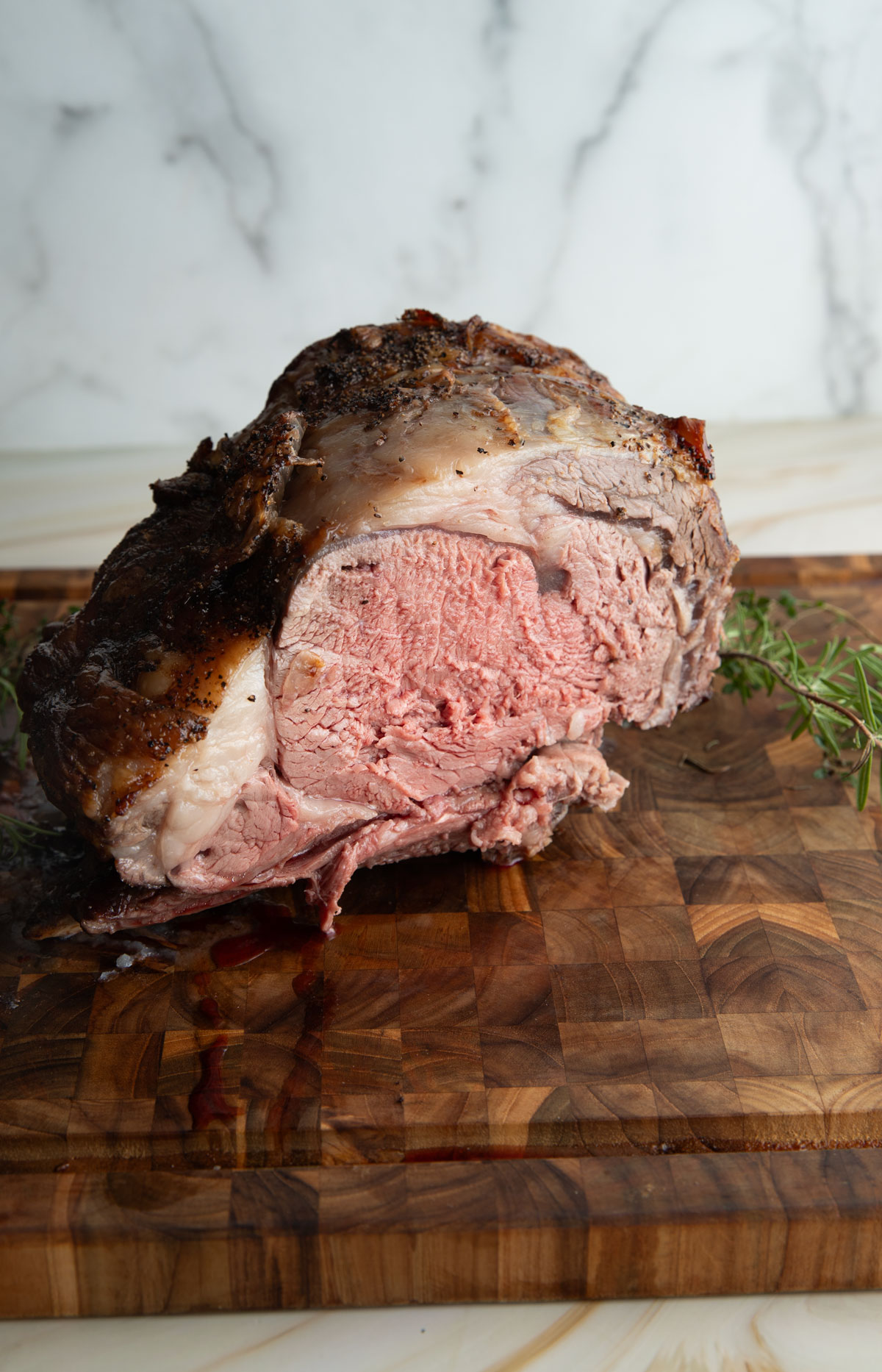 Sliced prime rib roast on a wooden cutting board with herbs.