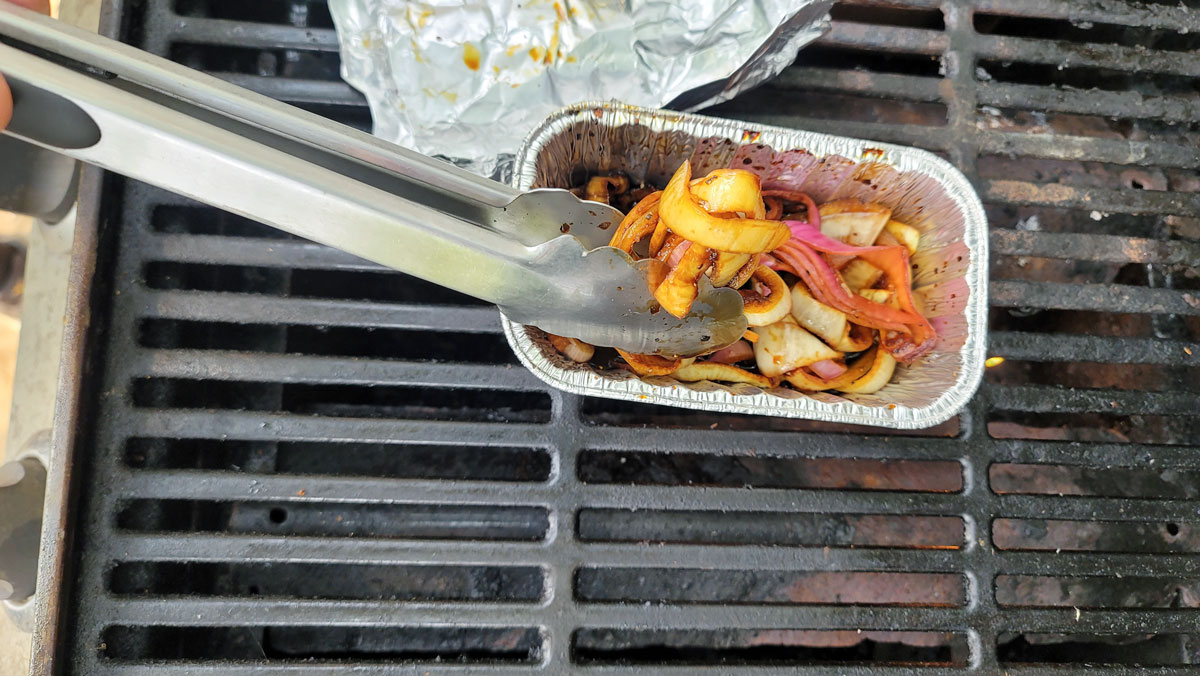 Flipping the onions with tongs on the grill.