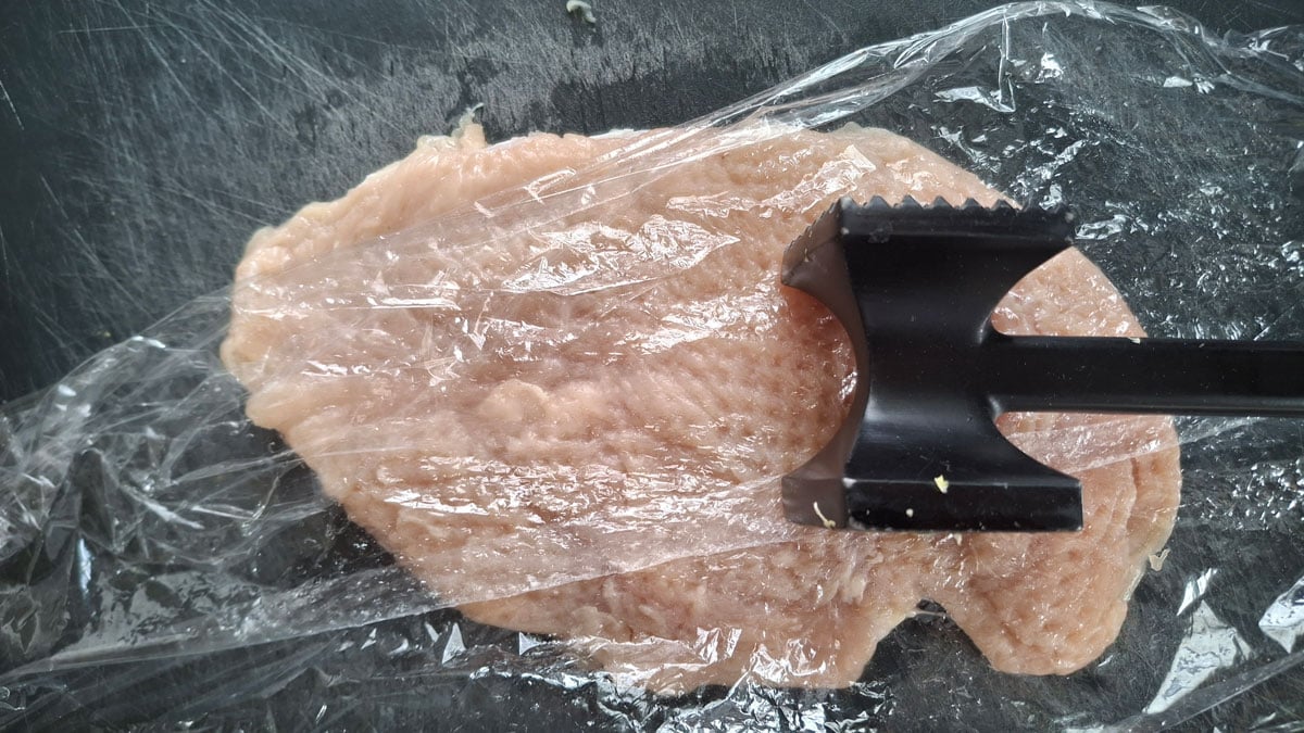 Chicken breast pounded out on a black cutting board.