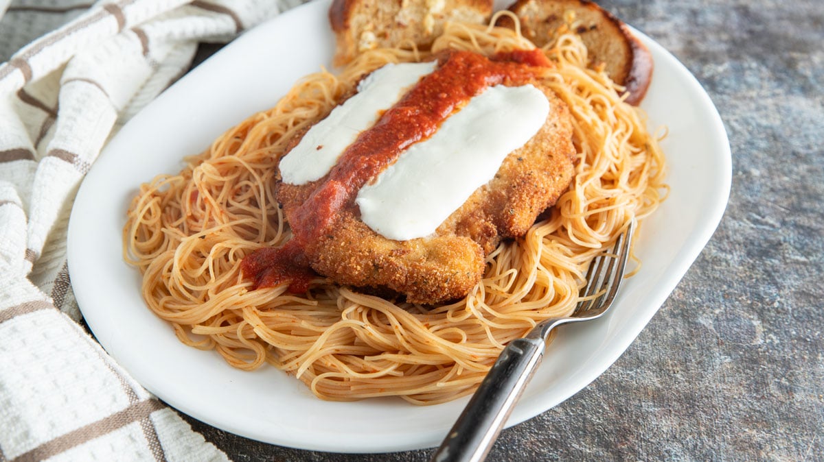 Large chicken breast parmesan on a bed of pasta.