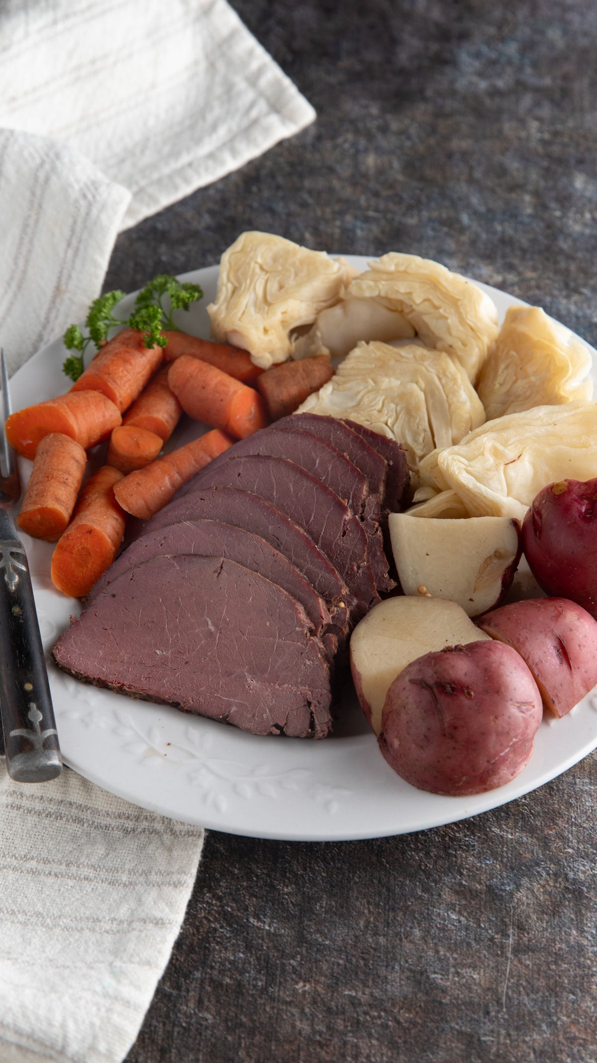 Corned venison and cabbage with carrots and potatoes on a white plate.