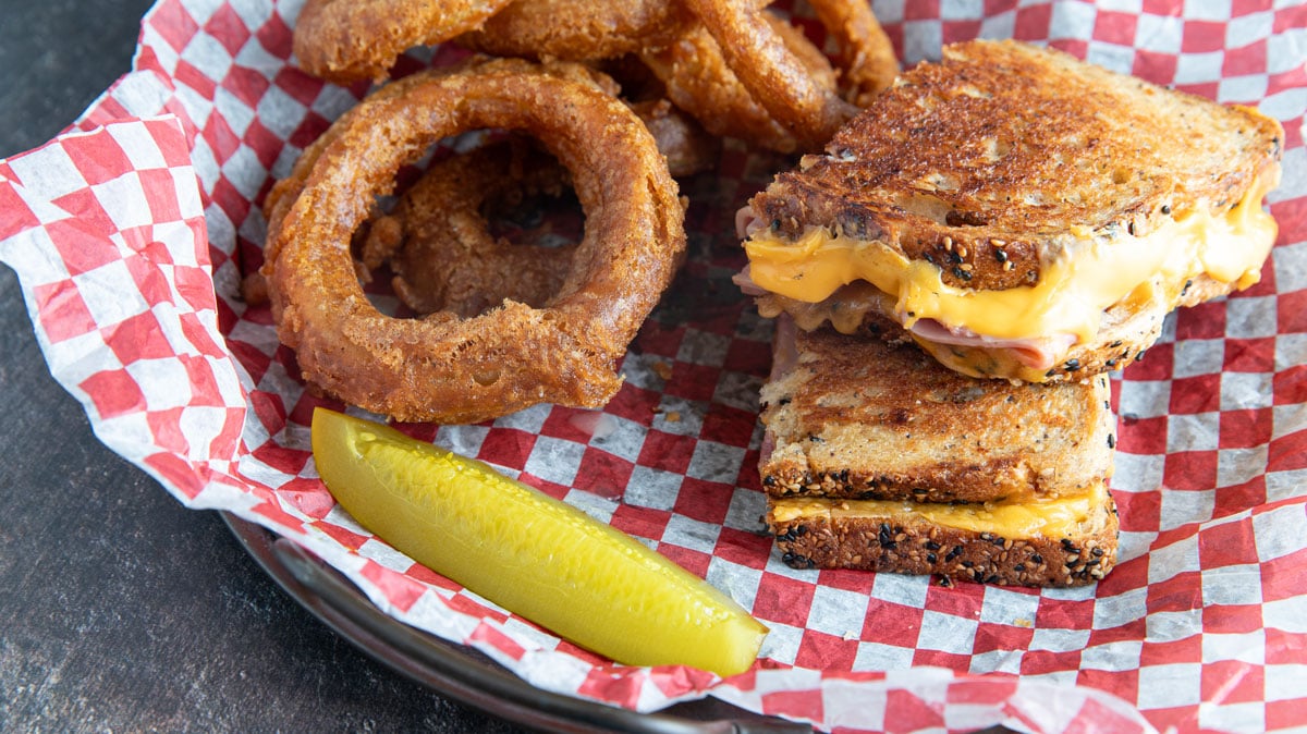 Grilled ham and cheese with onion rings and a pickle.