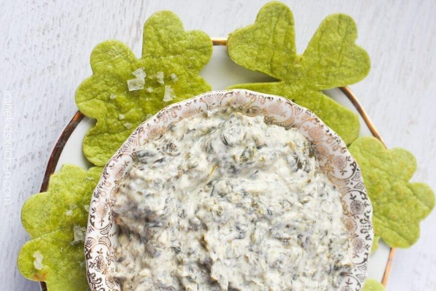An overhead shot of a bowl full of dip with shamrock-shaped chips surrounding it