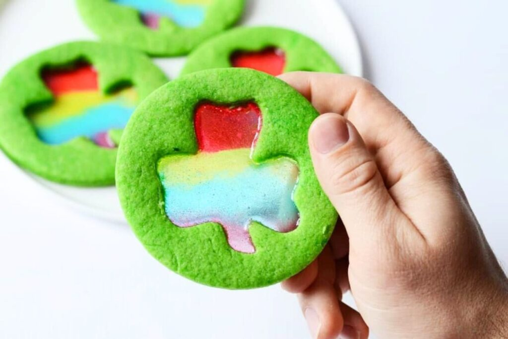 A hand holding a Stained Glass Shamrock Cookie on top of a platter of cookies.