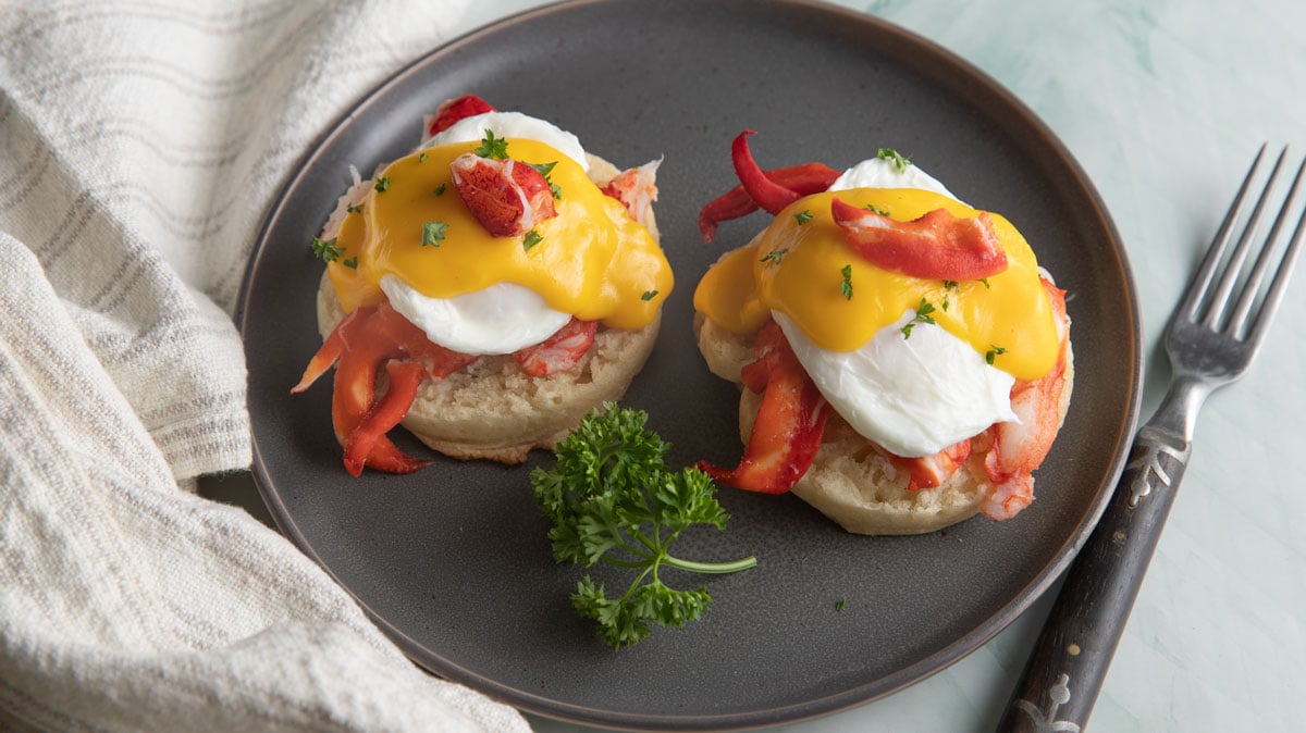 Lobster Benedict on a gray plate with parsley garnish.
