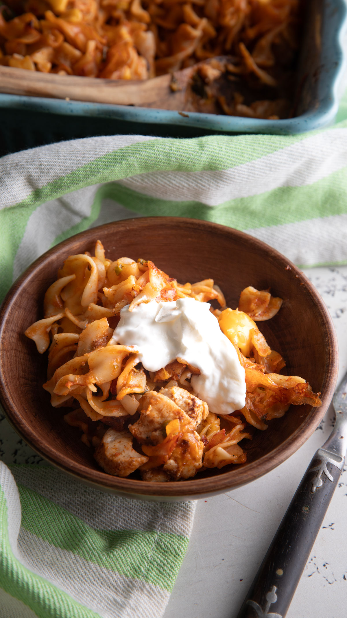 Wooden bowl filled with Mexican noodle casserole topped with sour cream.