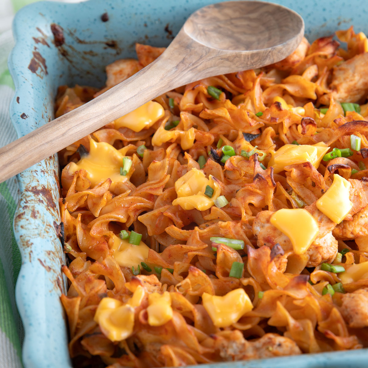 Mexican noodle casserole with dots of melted cheese in a green cassrole dish.