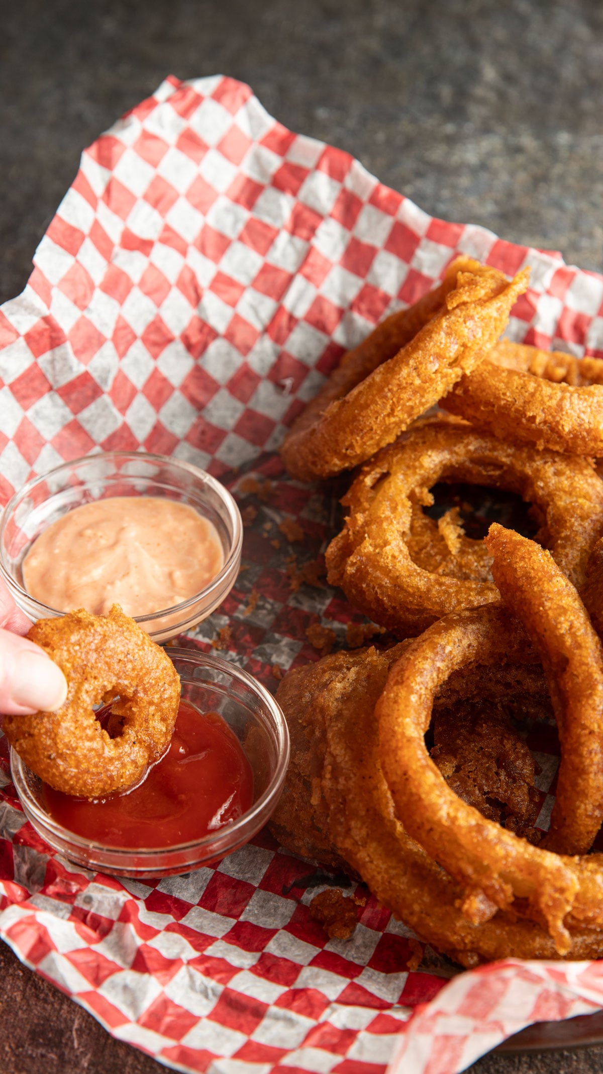 Dipping onion ring in a bowl with ketchup.