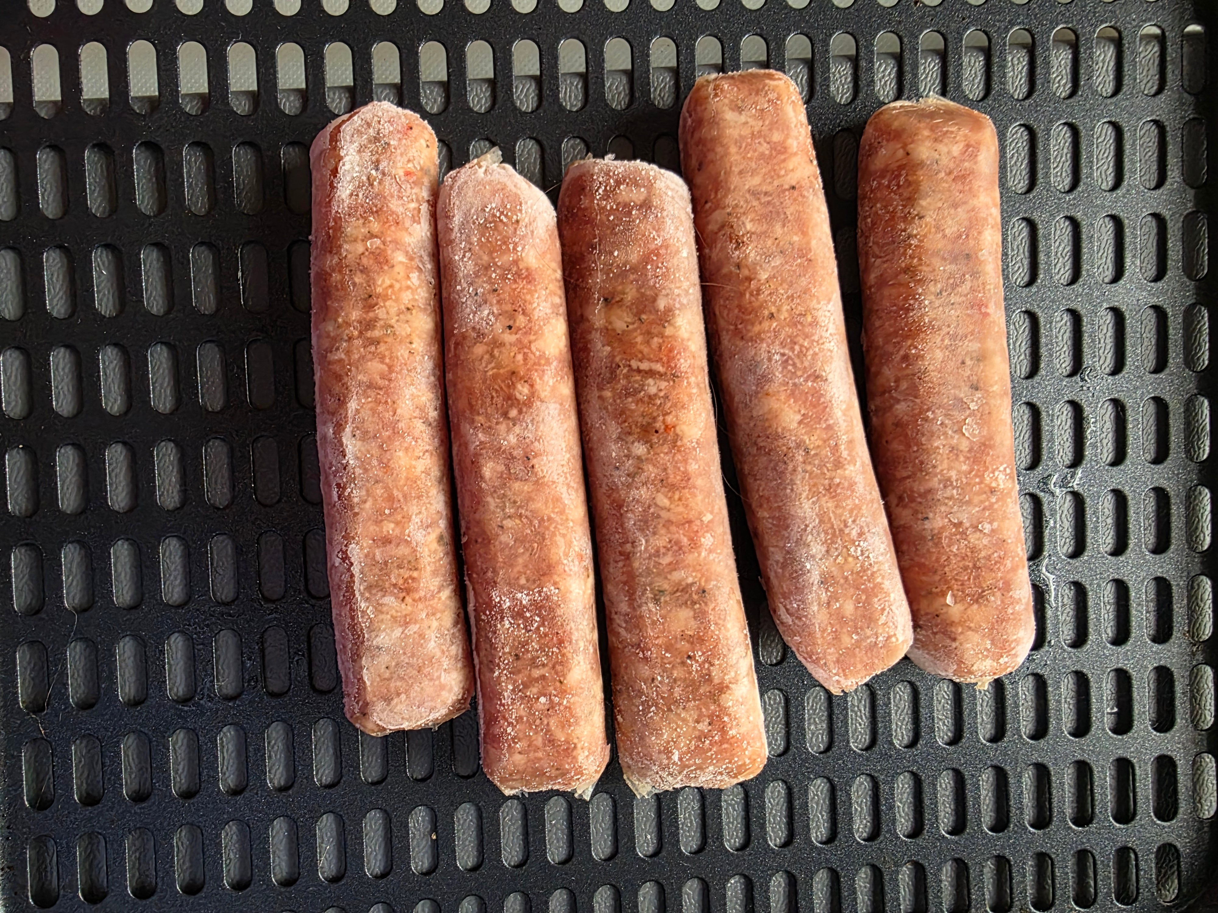 Frozen breakfast sausage in an air fryer basket.