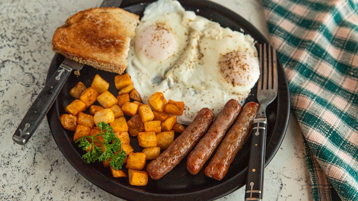 Air fryer breakfast sausage on a black plate with hashbrowns and fried eggs and toast.