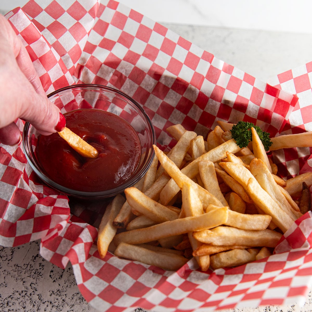 Woman's hand dipping a French fry in a bowl fo ketchup.