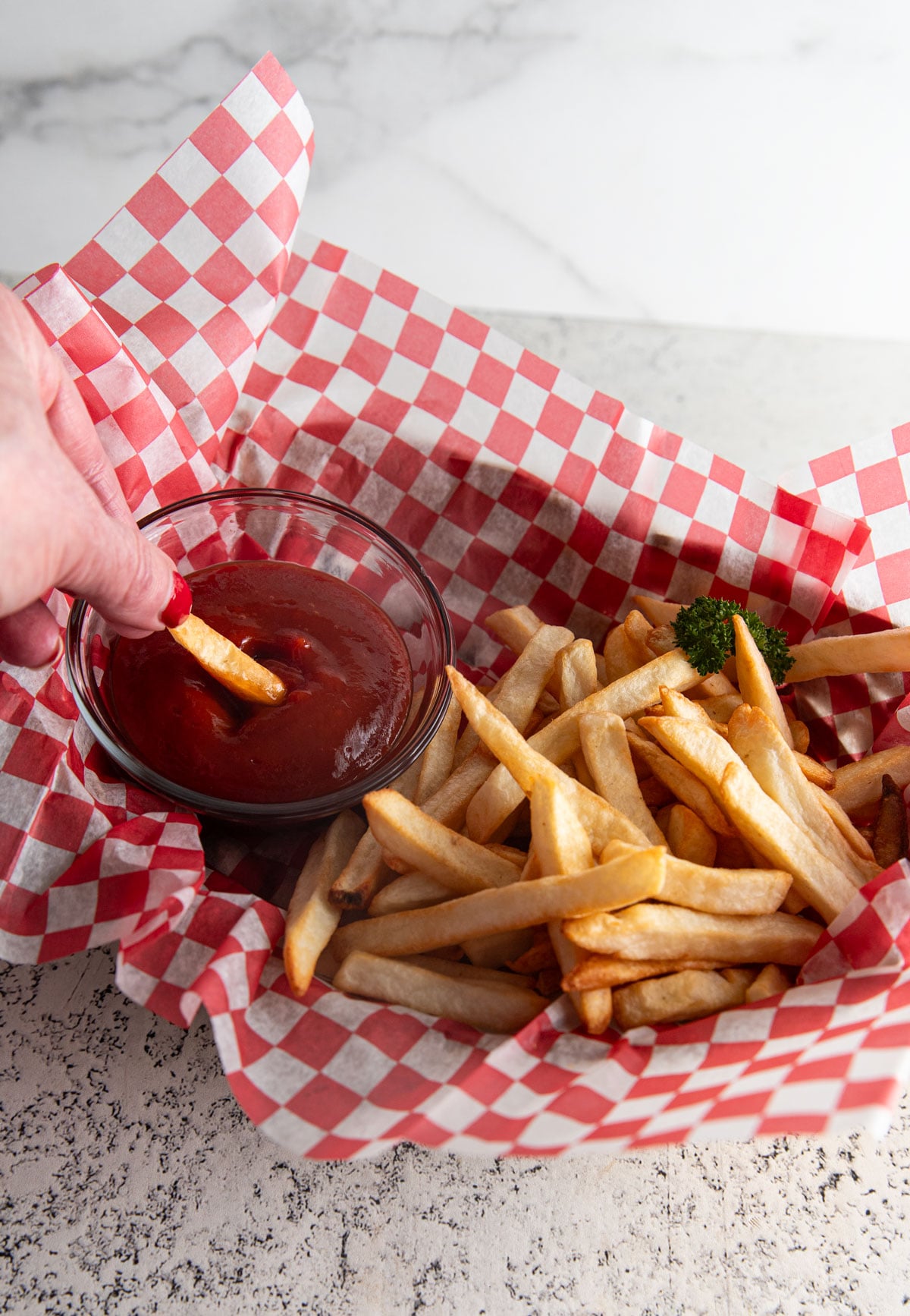 Woman's hand dipping a French fry into a bowl of ketchup.