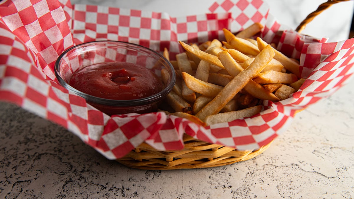 BAsket of French fries with a mall bowl of ketchup.
