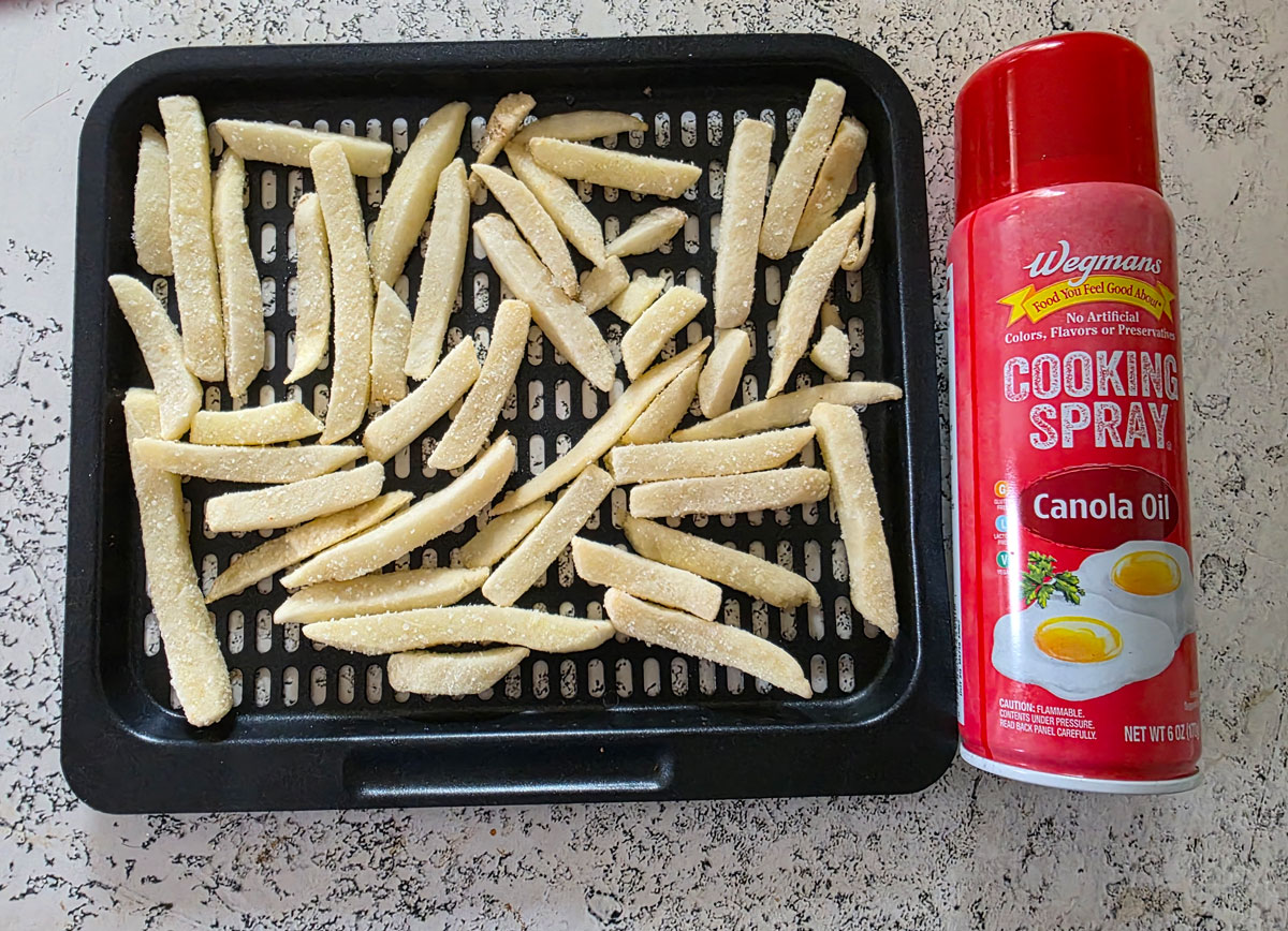 Air fryer basket with French Fries abd a spray can of cooking spray.