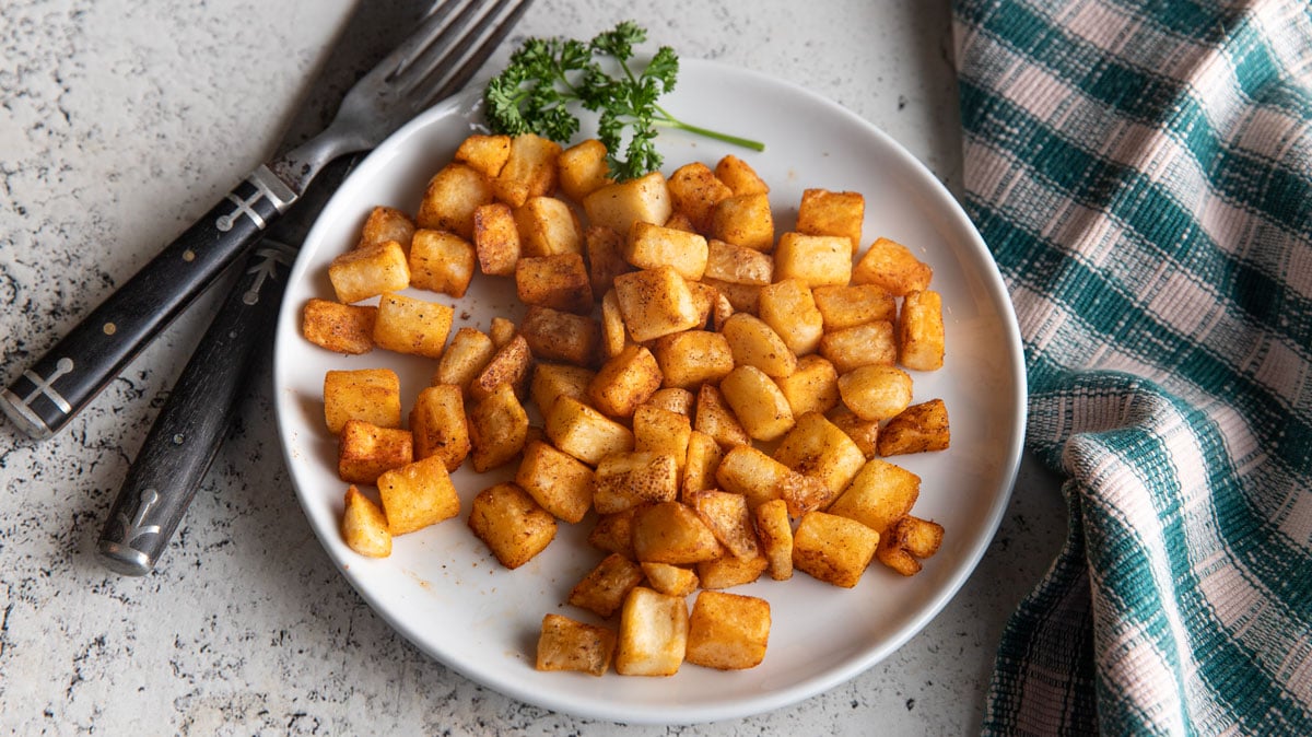 Golden air fryer hash browns on a white plate with parsley.