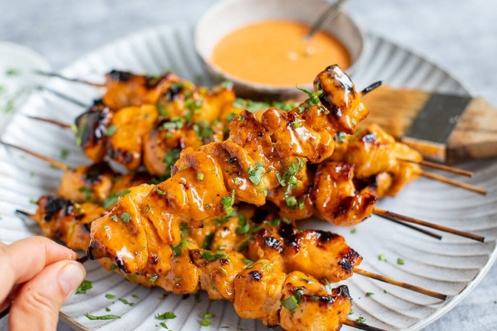 Bang Bang Chicken Skewers on a plate with sauce on the side.