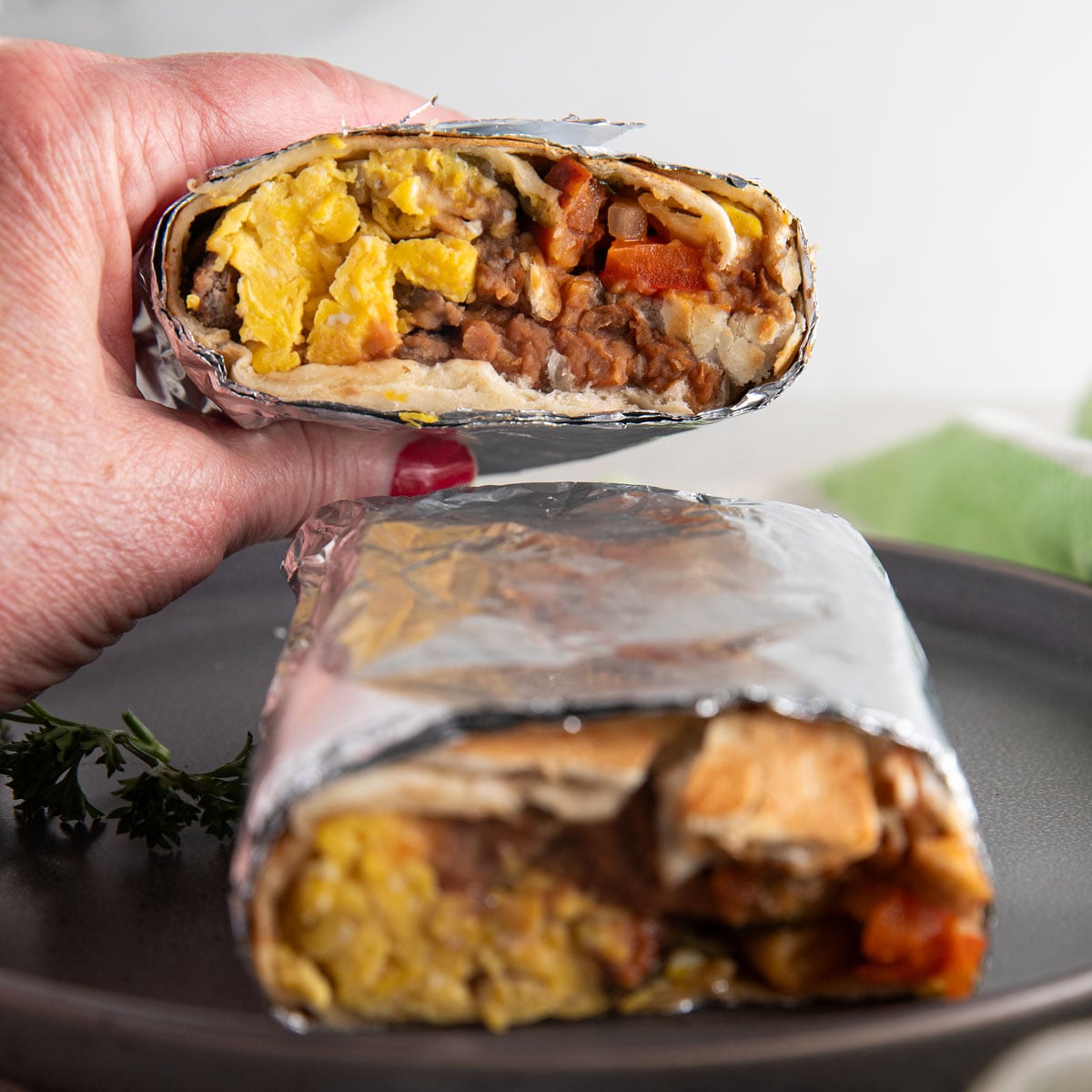 Womn's hand holding half of a burrito.