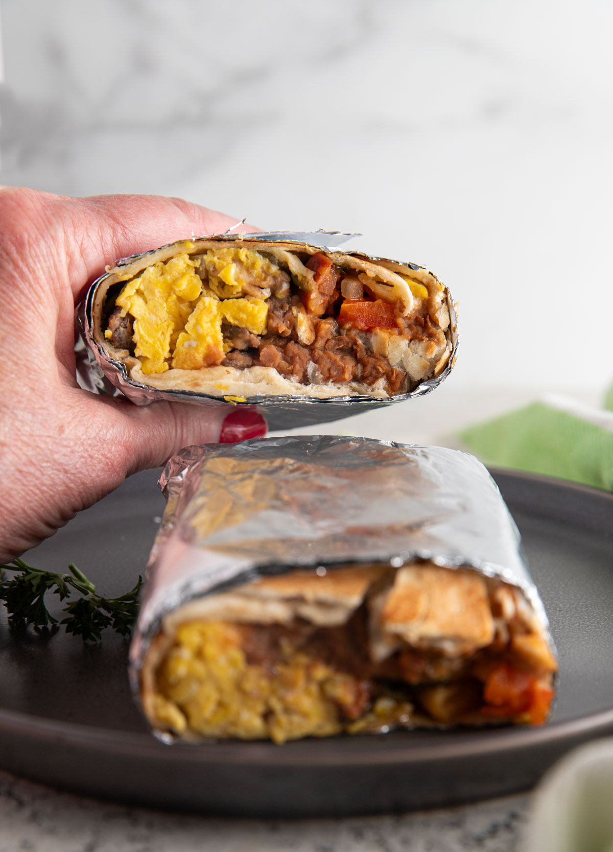 Woman's hand holding wrapped burrito. 
