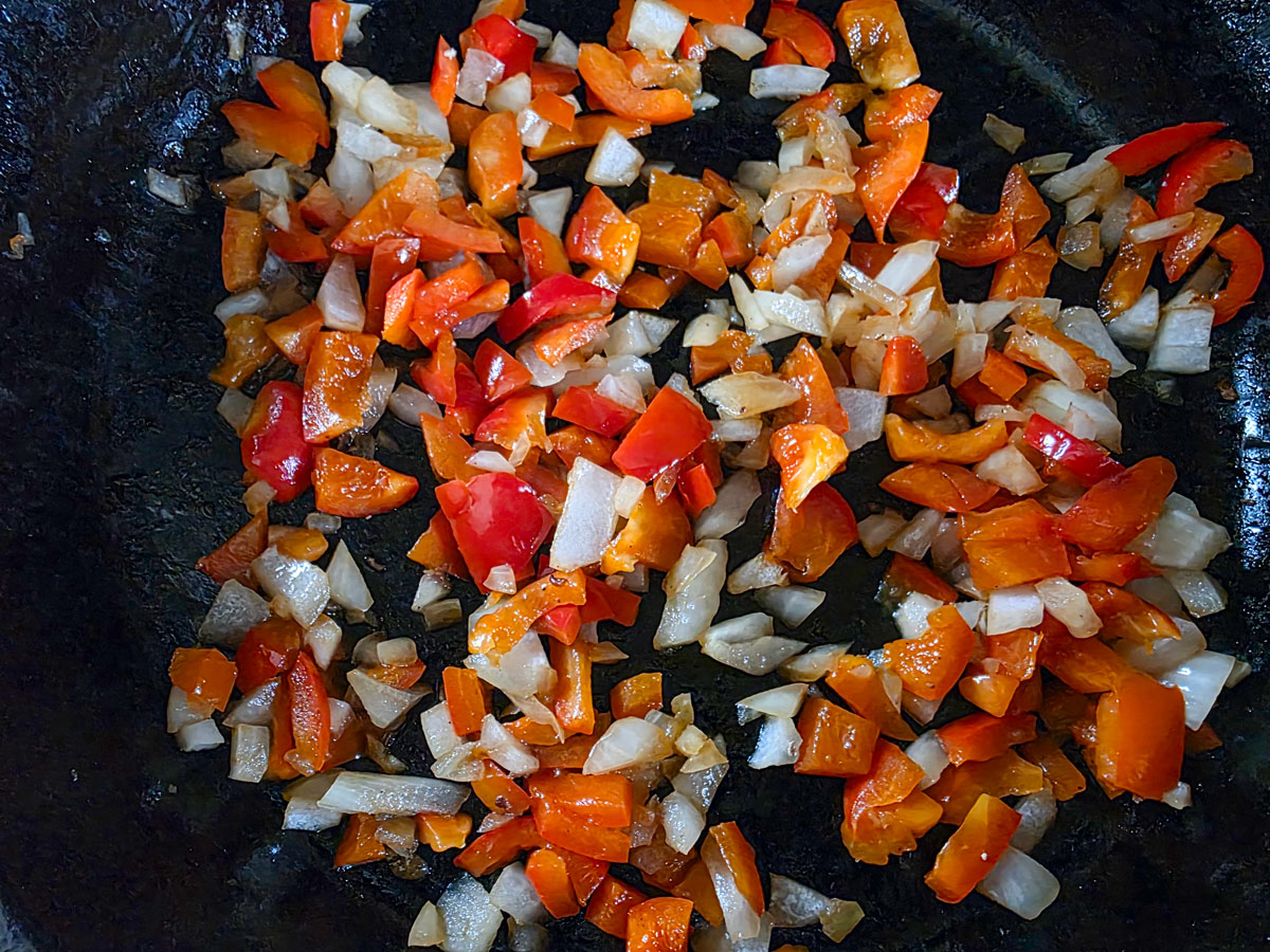 Diced peppers and onions in a cast iron skillet.