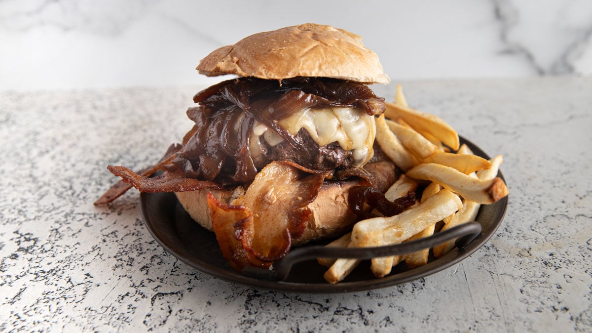 Caramelized onion burger on a black plate with fries.