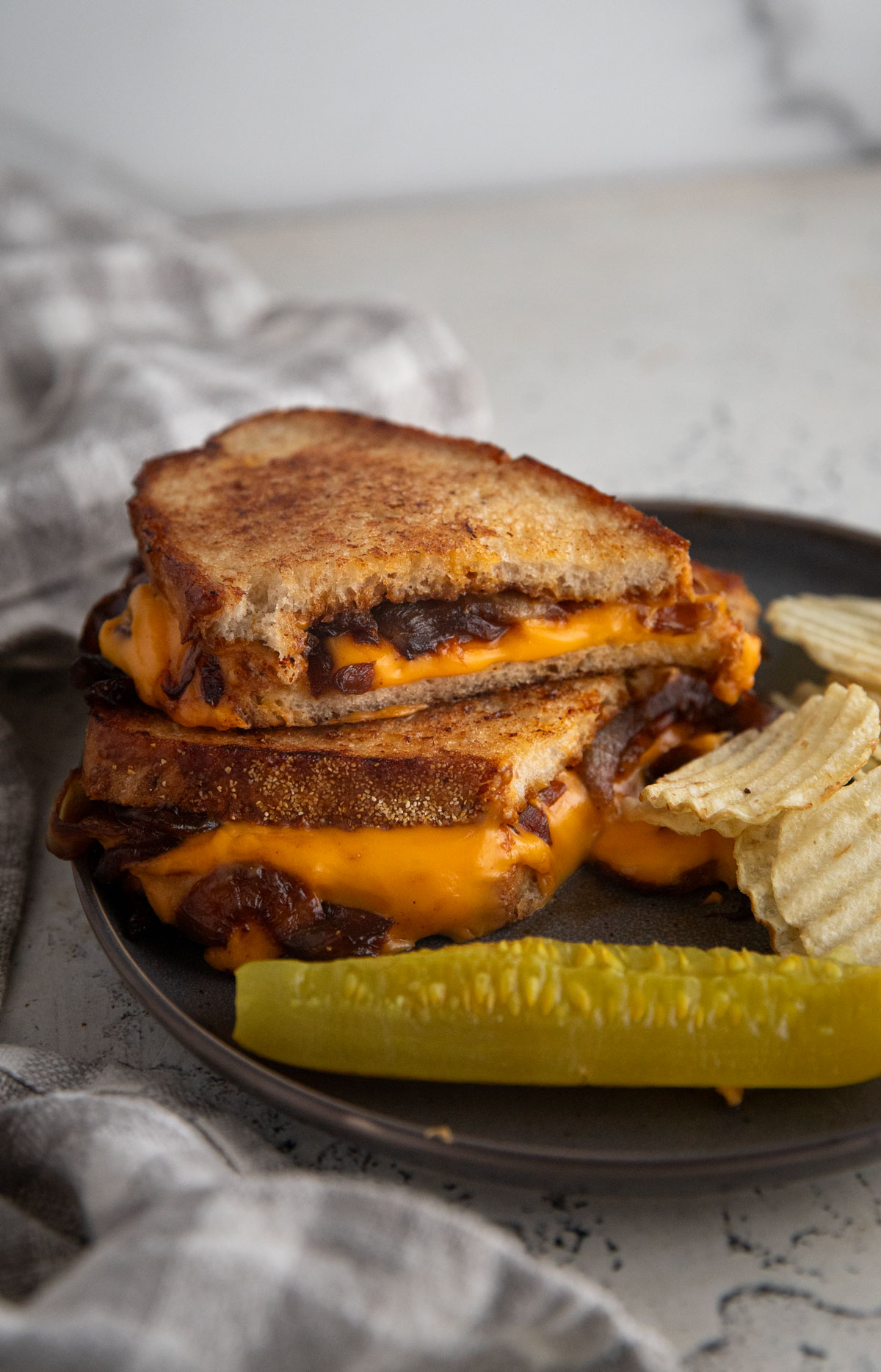 Caramelized onion grilled cheese on a plate wth chips and a pickle.