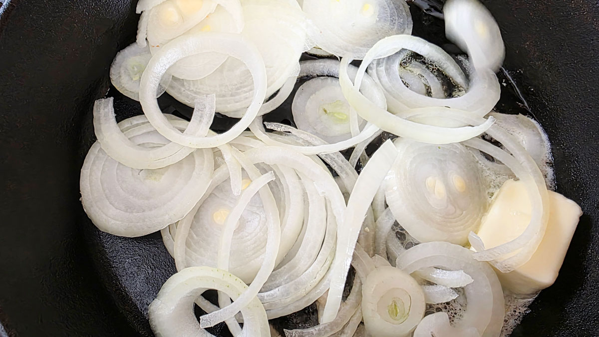 Sliced onions in a cast iron skillet with buter and oil.