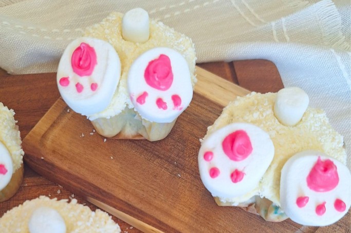 Two Easter Bunny Butt Cupcakes on a wooden chopping board.