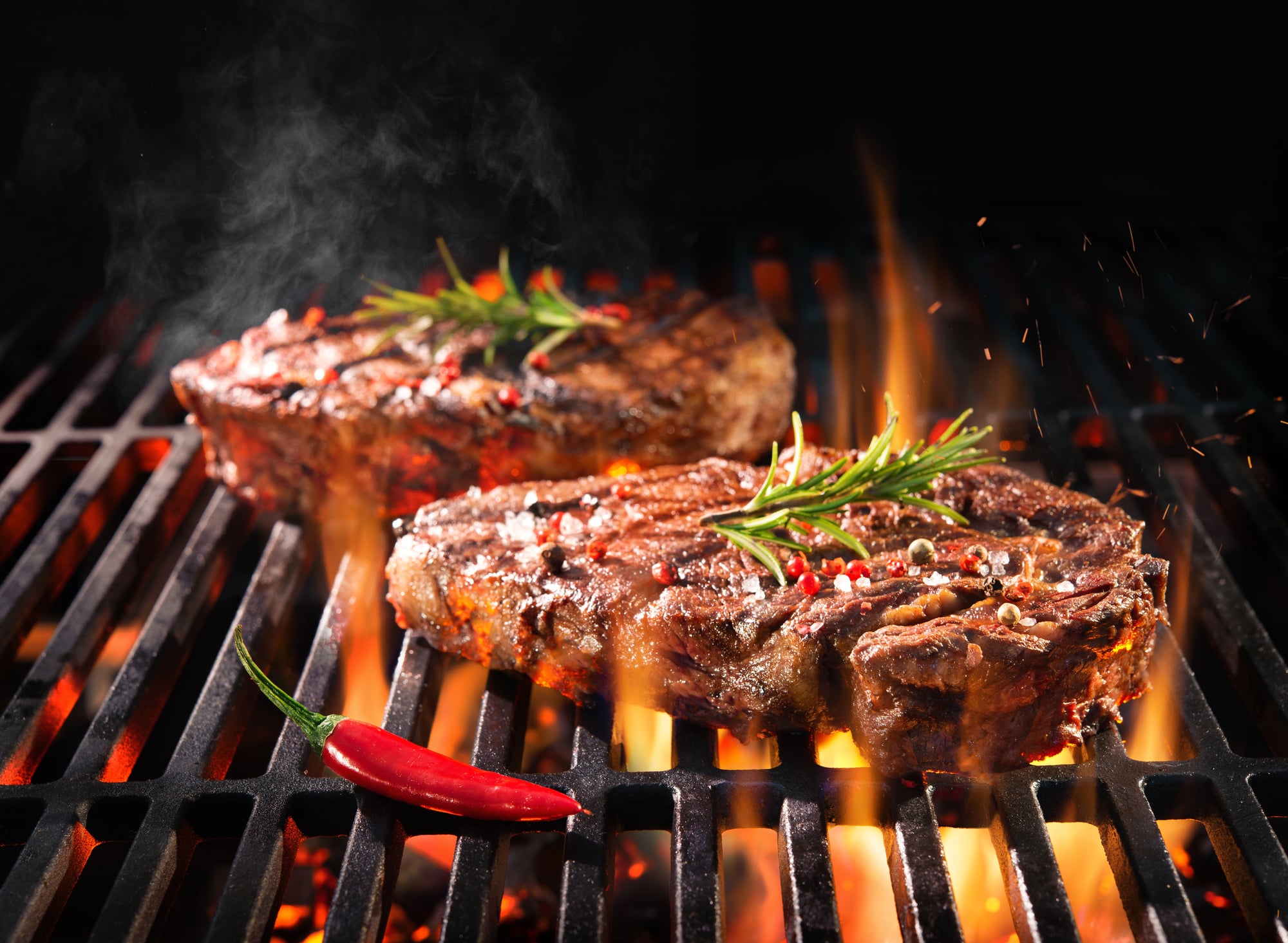 Two steaks on a grill with a serrano pepper.