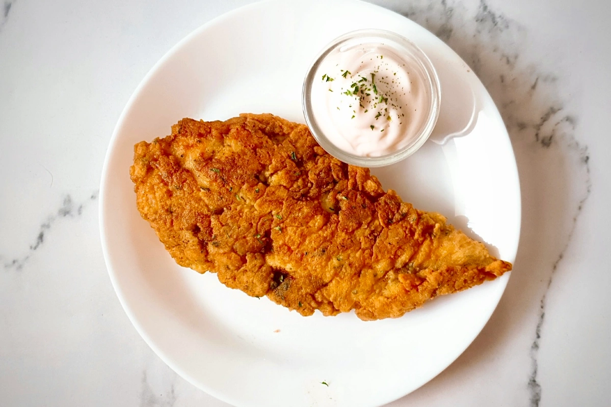 A plate of Best Fried Chicken Breast with dipping sauce on the side.