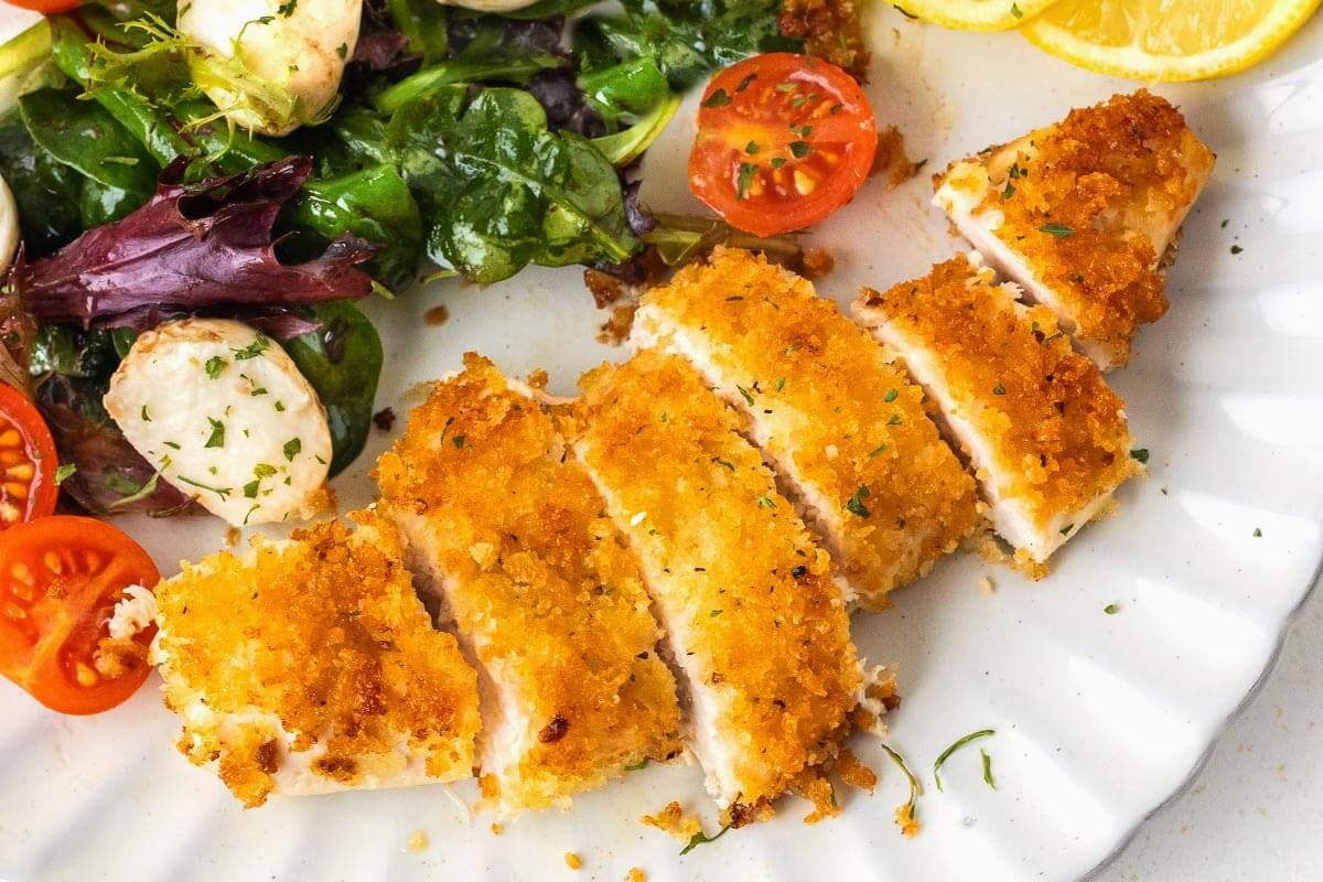 An overhead shot of cut-up Crispy Pan-Fried Chicken Cutlets with vegetables on the side.
