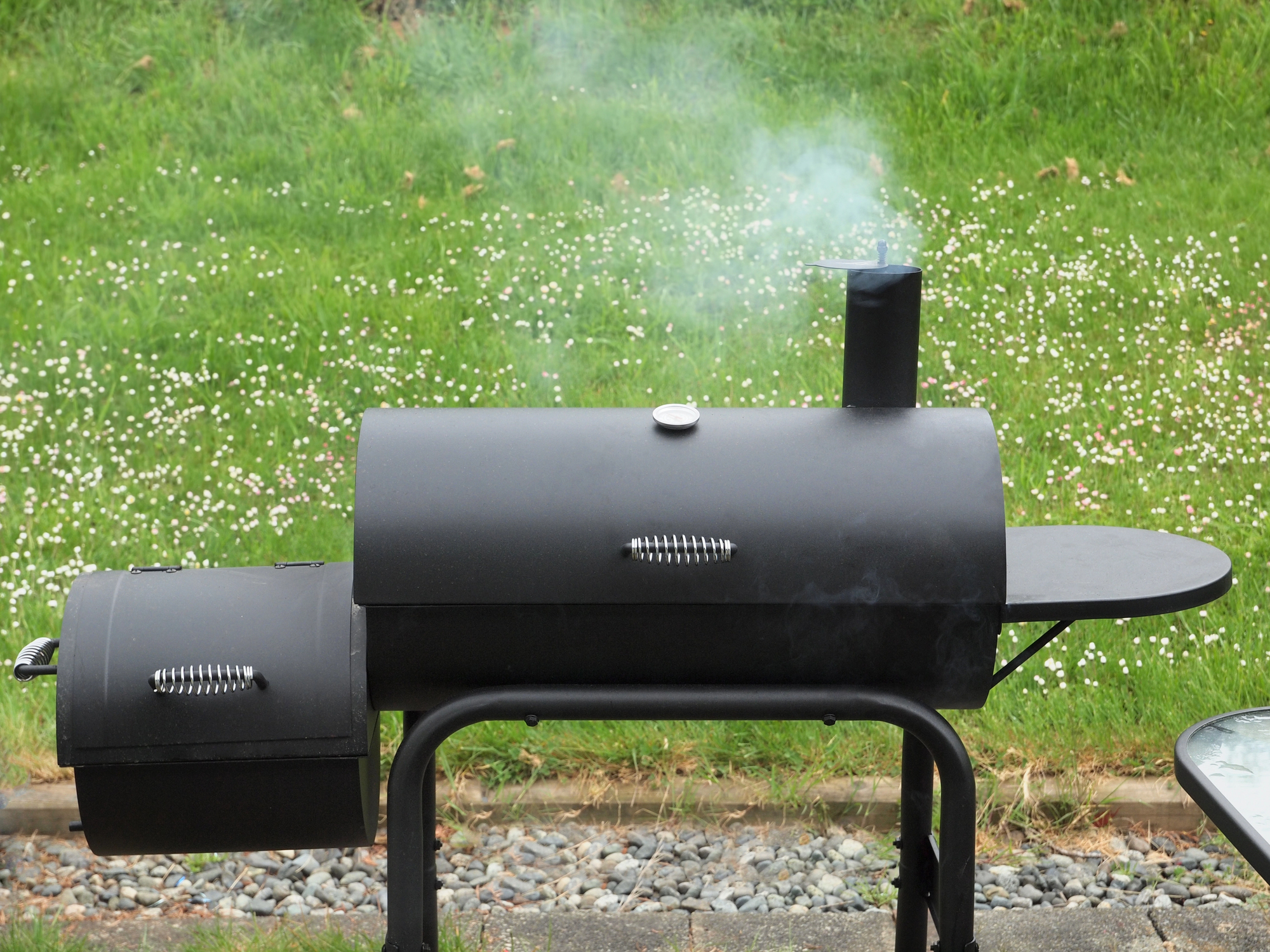 Offset smoker with grass in the background.