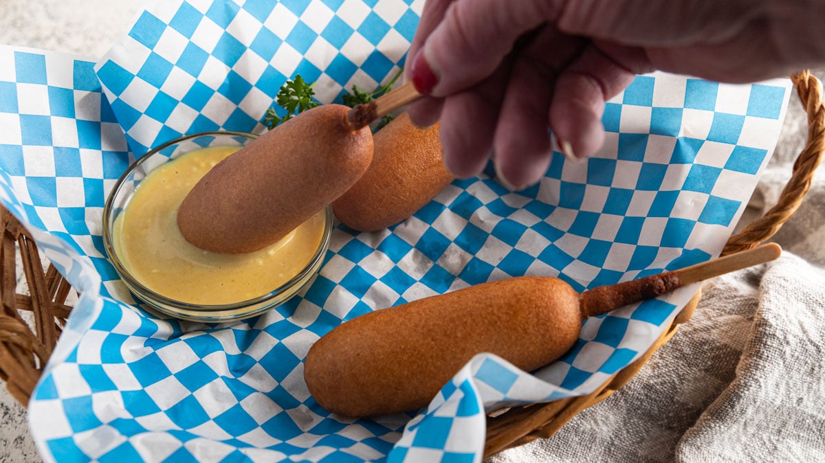 Woman's hand dipping a corn dog into a bowl of honey mustard.