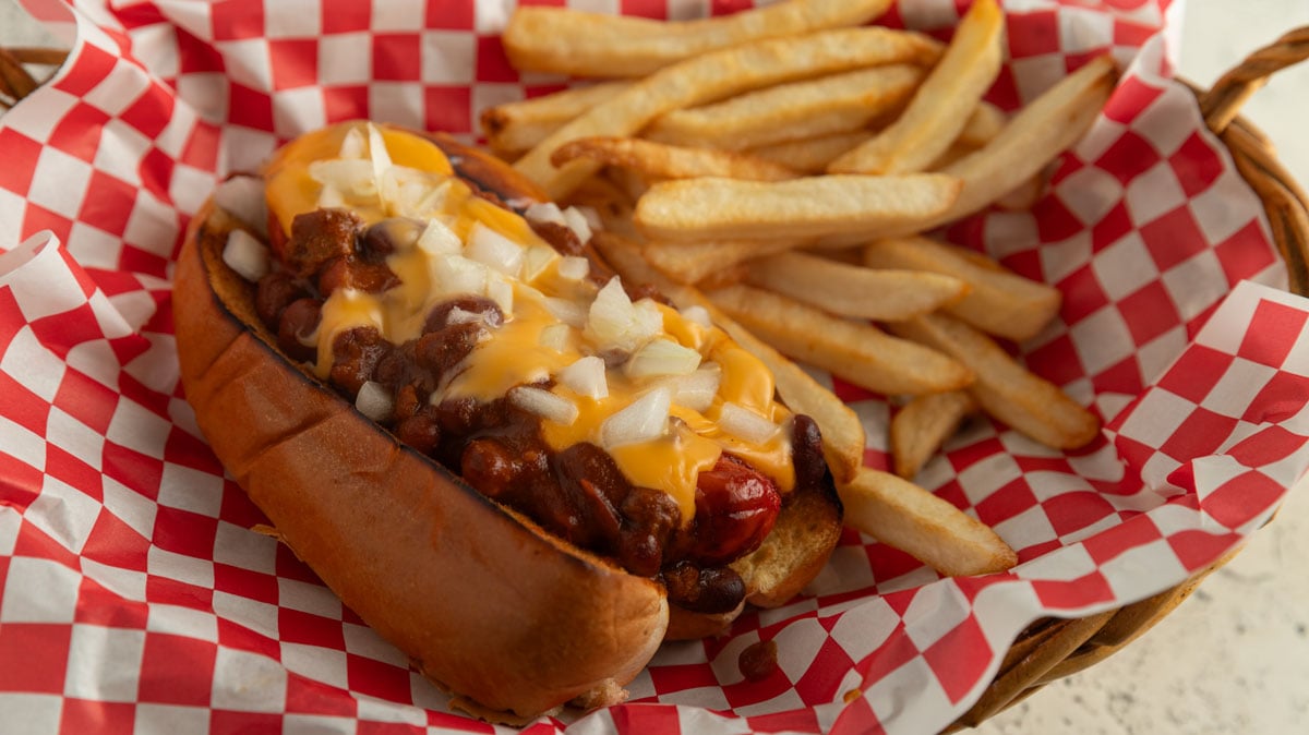 Chili cheese dog in a basket with browned fries.