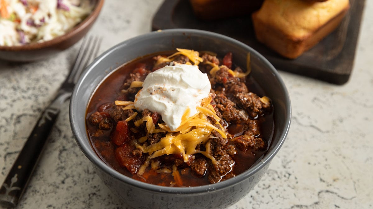 LBJs chili in a gray bowl topped with grated cheese and sour cream.